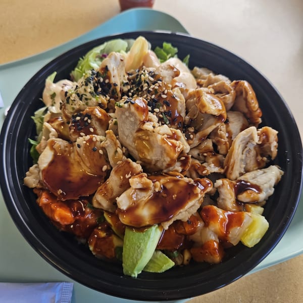 Teriyaki chicken bowl with sesame seeds, avocado, and pineapple, served on a light blue tray.