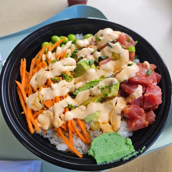 A colorful poke bowl with tuna, avocado, carrots, edamame, and sauce, with a side of wasabi.